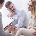 Upset young woman talking to a female psychologist with her husband aside